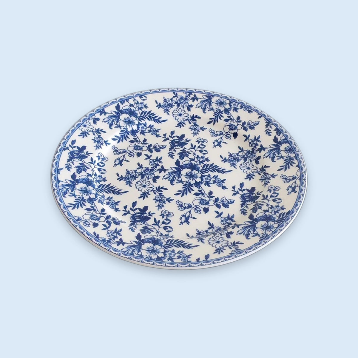 A white plate covered in blue floral patterns with a matching decorative rim sits against a pale blue background.