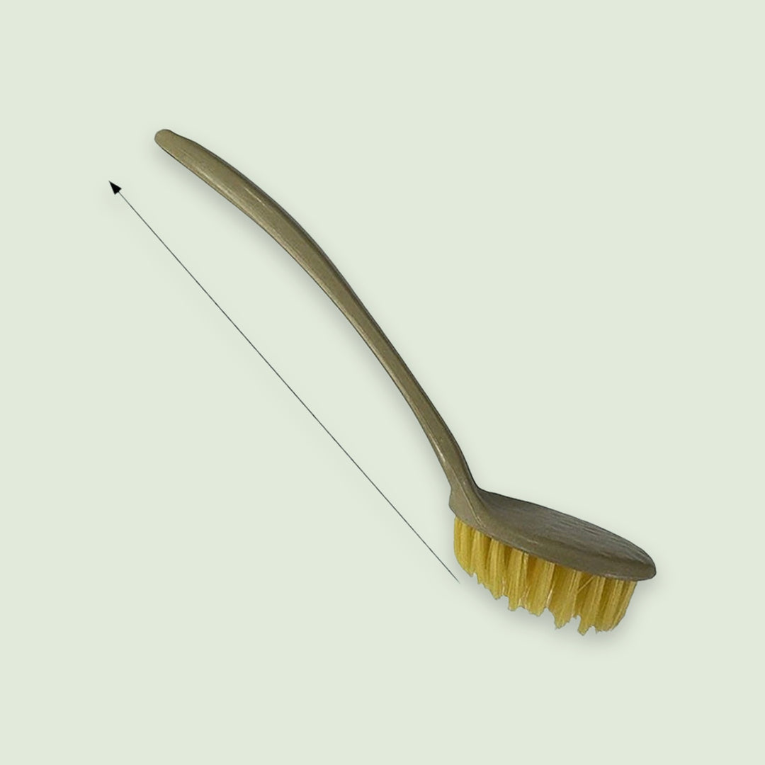 An olive-green dish brush with a curved handle and yellow bristles lies on a pale background beside an unlabelled measurement arrow.