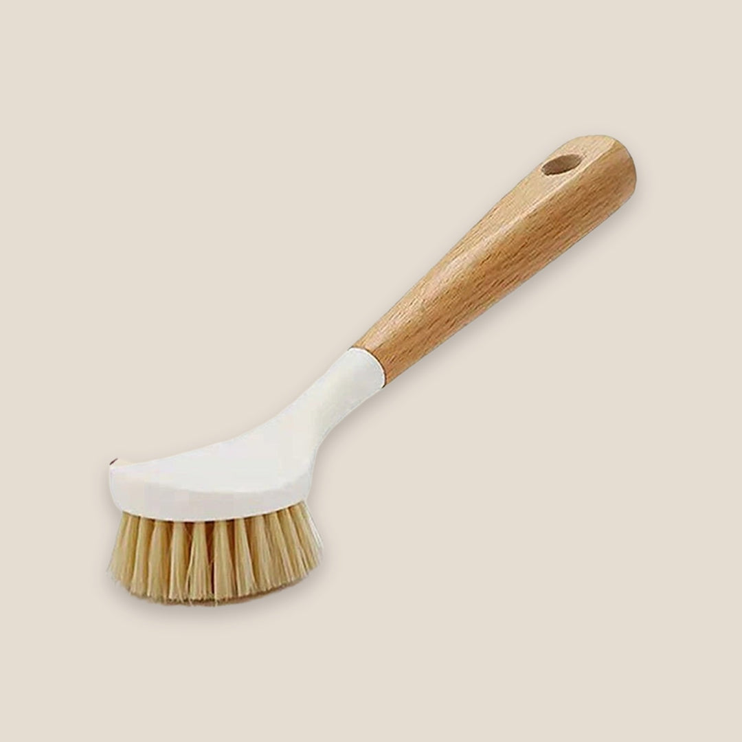 A dish brush with a white head, tan bristles and a wooden handle with a hanging hole rests on a beige background.