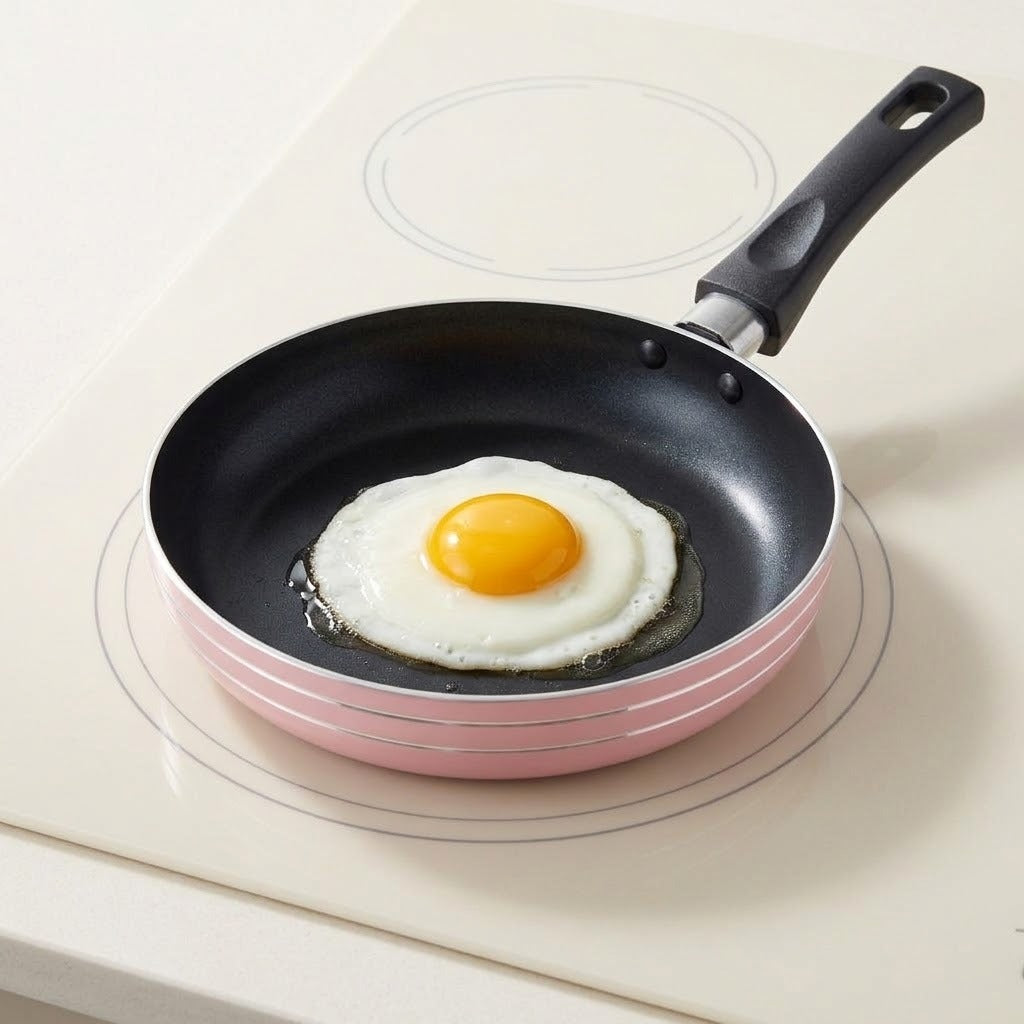 A pink frying pan with a black interior and handle holds a fried egg on a cream stovetop.
