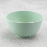 An empty pale green speckled bowl with a raised circular base sits on a light grey textured surface.