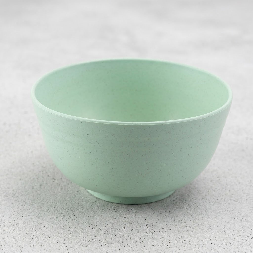 An empty pale green speckled bowl with a raised circular base sits on a light grey textured surface.