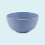 An empty blue speckled bowl with rounded sides and a small circular base sits against a pale blue background.