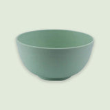 An empty green speckled bowl with rounded sides and a small circular base sits against a pale green background.