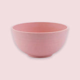 An empty pink speckled bowl with rounded sides and a small circular base sits against a pale pink background.