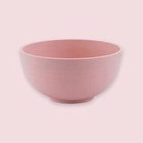 A pink bowl with rounded sides and a raised circular base sits against a pale pink background.