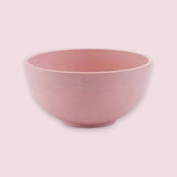 A pink bowl with an open top and rounded sides sits on a circular base against a pale pink background.