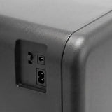 Close-up of a dark grey mini fridge’s textured casing, rounded corner, recessed switch, and two power sockets.