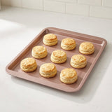 Rose-coloured rectangular baking tray holds nine golden biscuits on a white countertop against a white tiled backsplash.