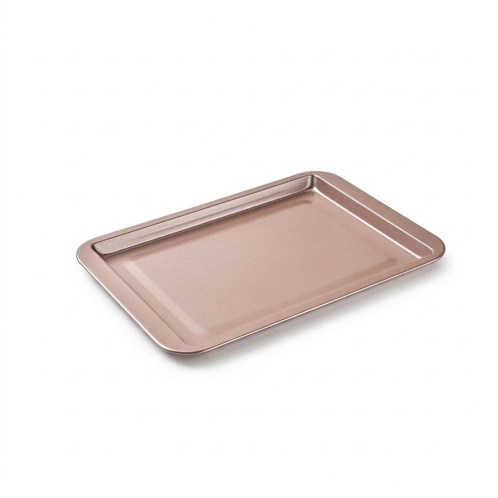 An empty rose-coloured rectangular baking tray with raised sides and rounded corners sits against a white background.