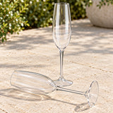 Clear Tritan plastic champagne flute lying intact on a stone patio beside an upright flute, showing it does not break