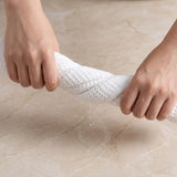Two hands wring water from a white waffle-textured cloth over a beige marble-patterned surface.