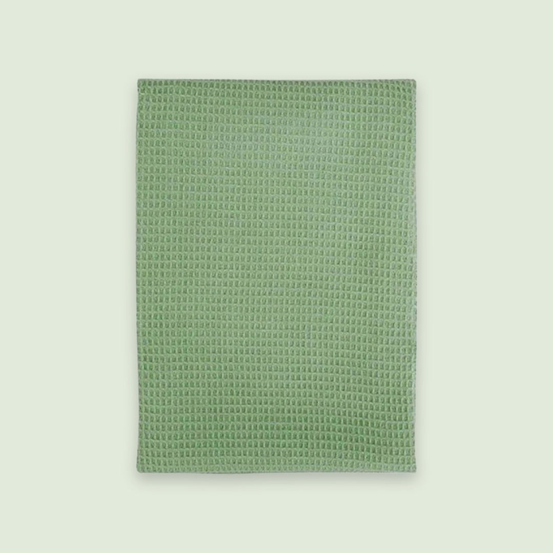 A rectangular sage green textured towel or mat with a raised waffle-like pattern, shown flat against a light off-white background.