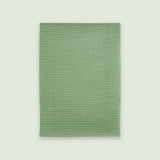 A rectangular sage green textured towel or mat with a raised waffle-like pattern, shown flat against a light off-white background.