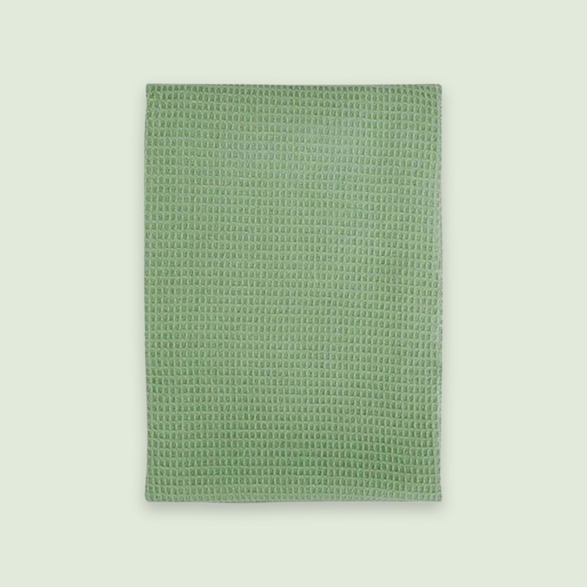 A rectangular sage green textured towel or mat with a raised waffle-like pattern, shown flat against a light off-white background.