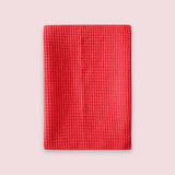 A red textured waffle-weave fabric sleeve or pouch, shown flat against a solid pale pink background.