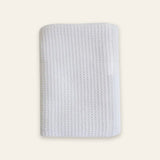 A white textured fabric pouch or sleeve with a waffle-like pattern, shown flat against a solid cream background.