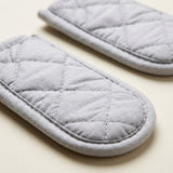 Two light gray quilted fabric oven mitts with diamond stitching, shown on a light beige background.