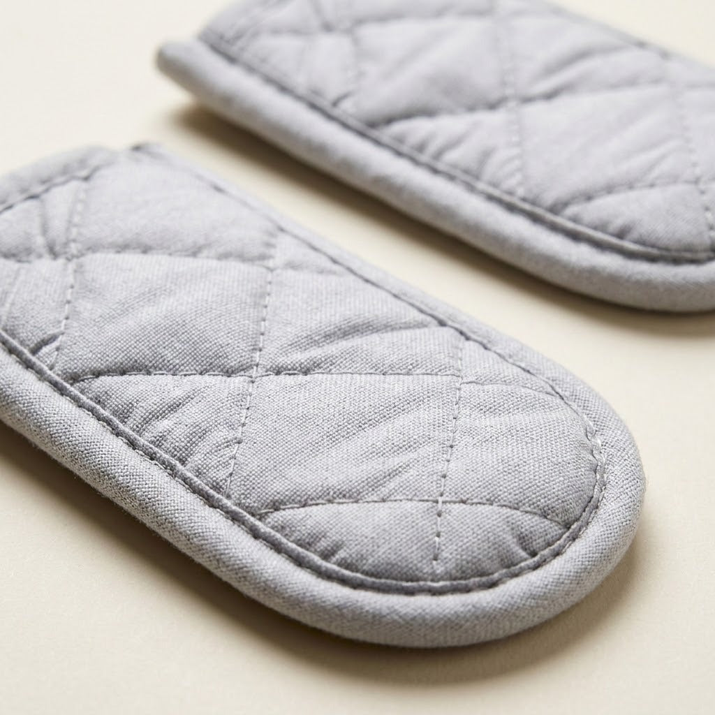Two light gray quilted fabric oven mitts with diamond stitching, shown on a light beige background.