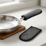 Black and white striped quilted sleeves beside a silver pan on a wooden board, with one sleeve fitted over its handle.
