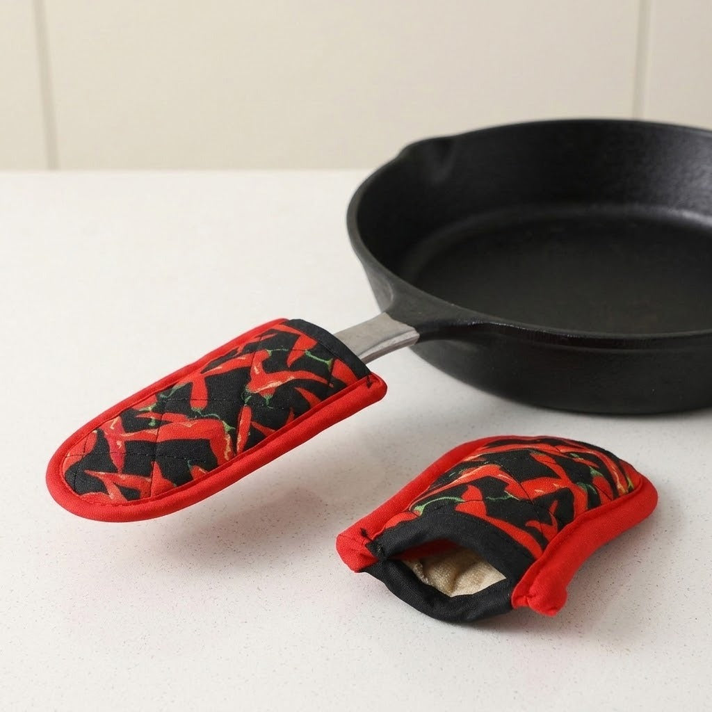 Red chili pepper print sleeves on a white countertop, one covering a black skillet handle and another showing its pale inner padding.