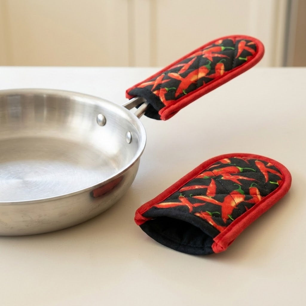 Two red chili pepper print fabric sleeves, one covering a silver pan handle and one resting on a cream countertop.