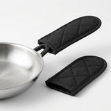 Two black quilted fabric sleeves on a white background, one fitted over a silver pan handle and the other lying beside it.