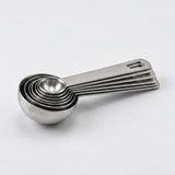 Silver stainless steel measuring spoons nest together with aligned flat handles on a plain light background.
