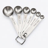 Six silver stainless steel measuring spoons fan out on white, with engraved capacities from 1/8 teaspoon to 1 tablespoon.