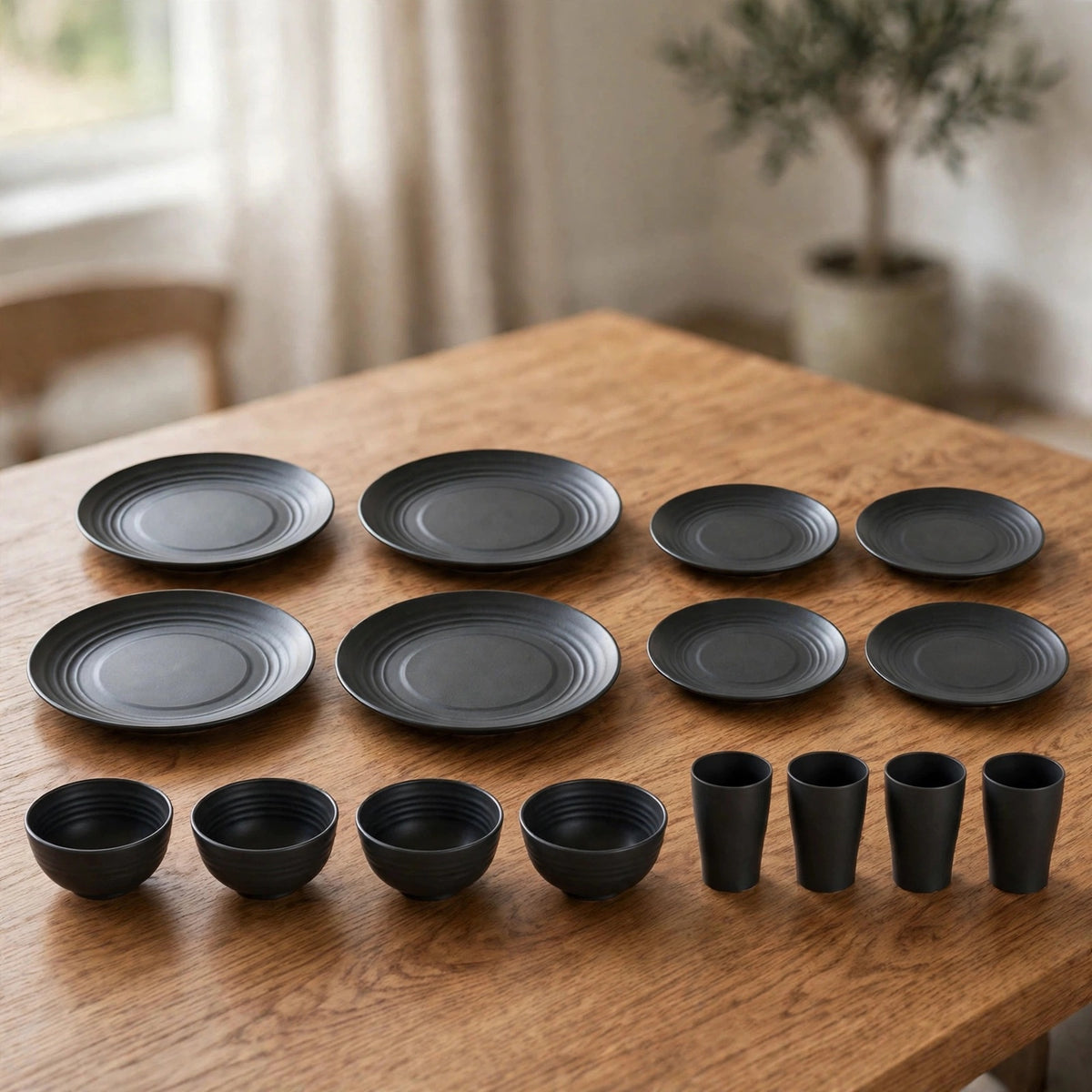 Sixteen-piece black dinnerware set with large plates, small plates, bowls, and cups laid out on a wooden table.