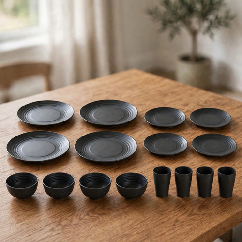 Sixteen-piece black dinnerware set with large plates, small plates, bowls, and cups laid out on a wooden table.