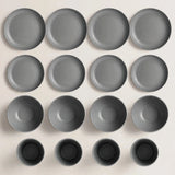 Grey dinnerware pieces arranged in rows on a cream background, including large plates, small plates, bowls, and cups.
