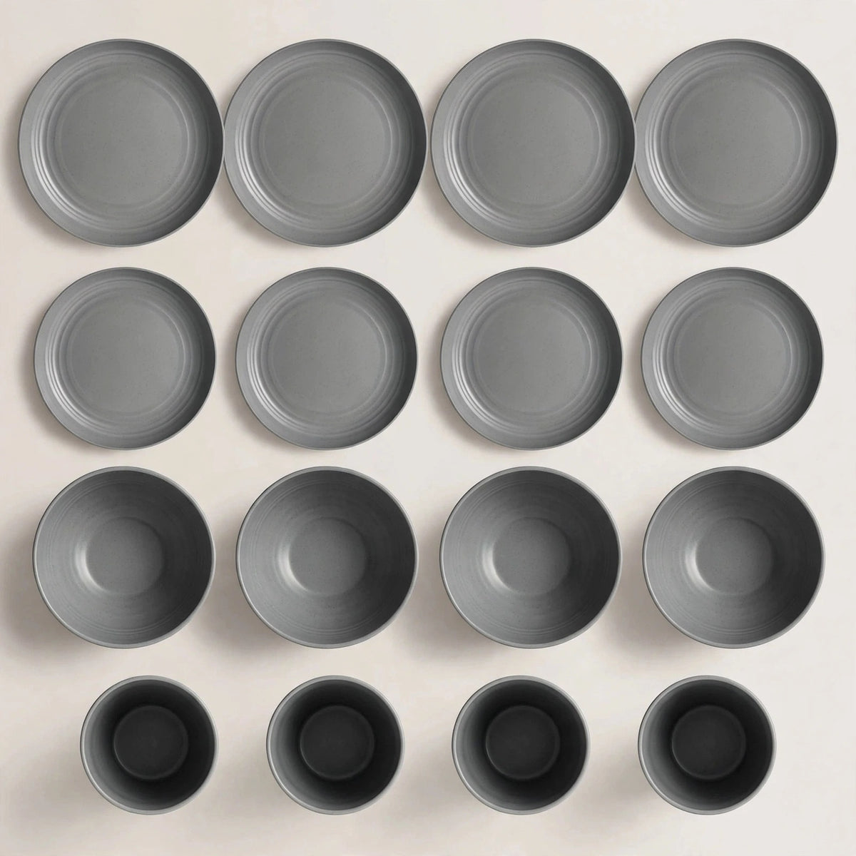 Grey dinnerware pieces arranged in rows on a cream background, including large plates, small plates, bowls, and cups.
