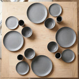 Grey wheat straw dinnerware set with plates, bowls, and cups arranged around a light wooden table, viewed from above.