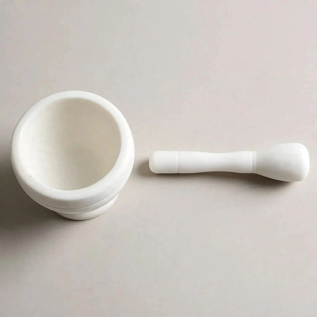 A white ceramic mortar and pestle set on a light beige background.