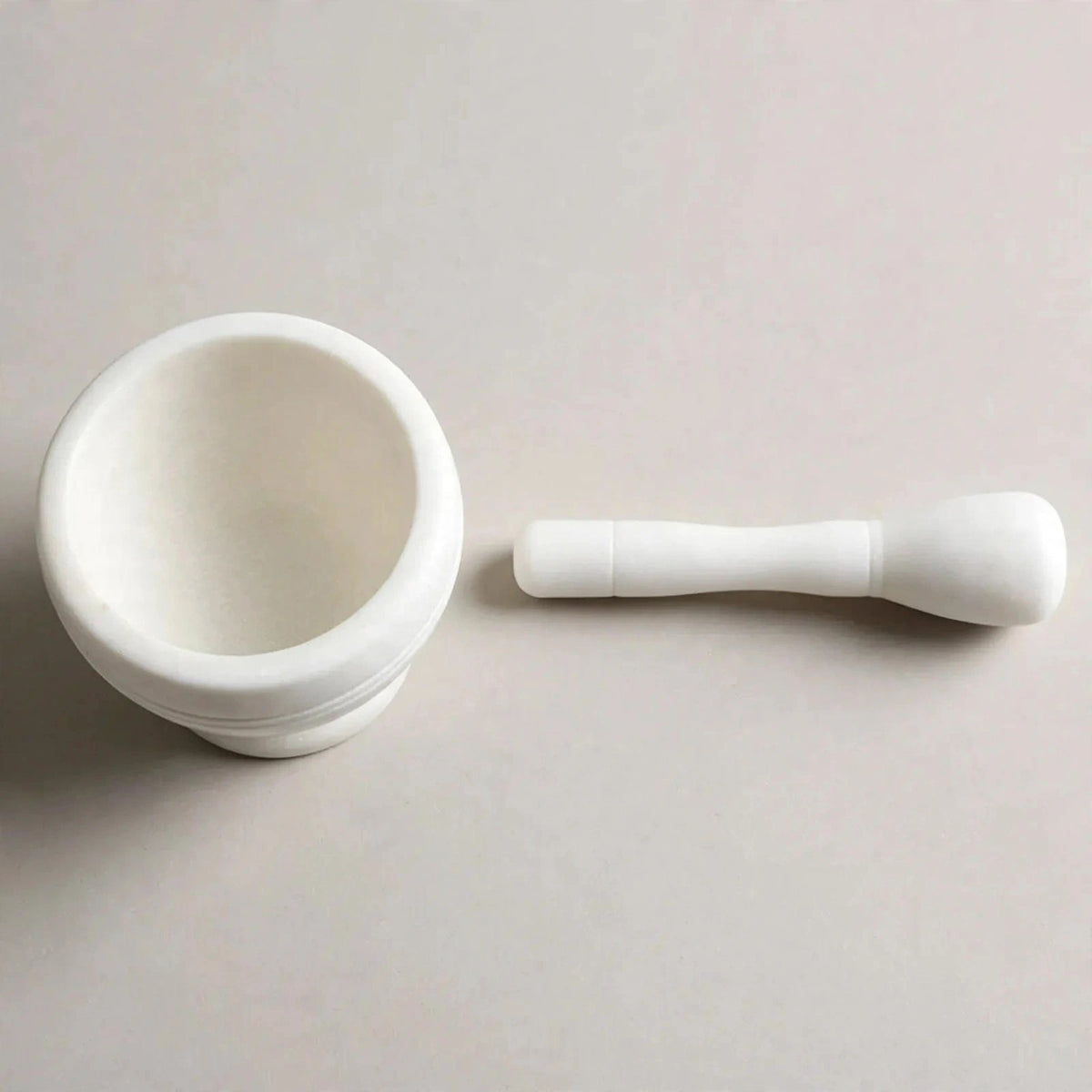A white ceramic mortar and pestle set on a light beige background.