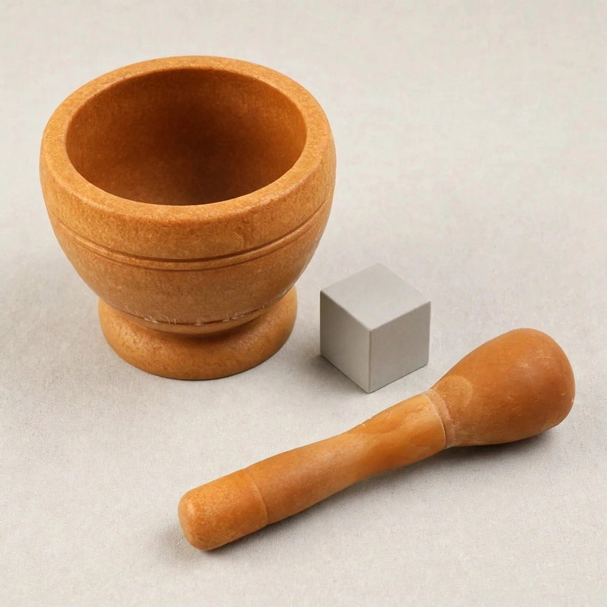 Brown wooden mortar and pestle arranged separately beside a small grey cube on a light grey background.