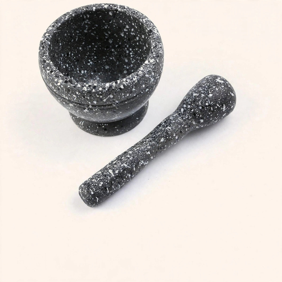 Empty black mortar with white speckles and matching pestle placed diagonally beside it on an off-white background.