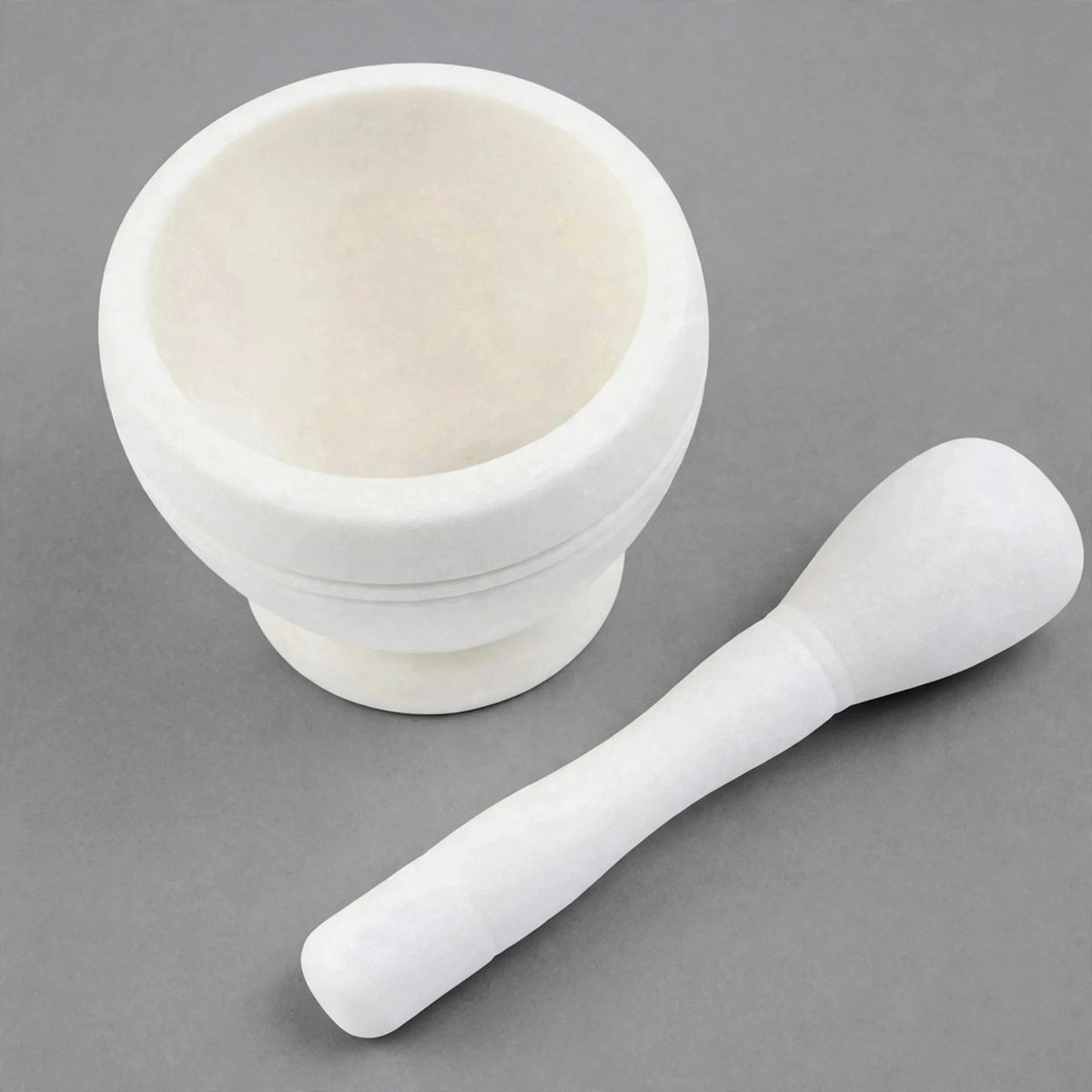 A white marble mortar and pestle set on a neutral gray background.