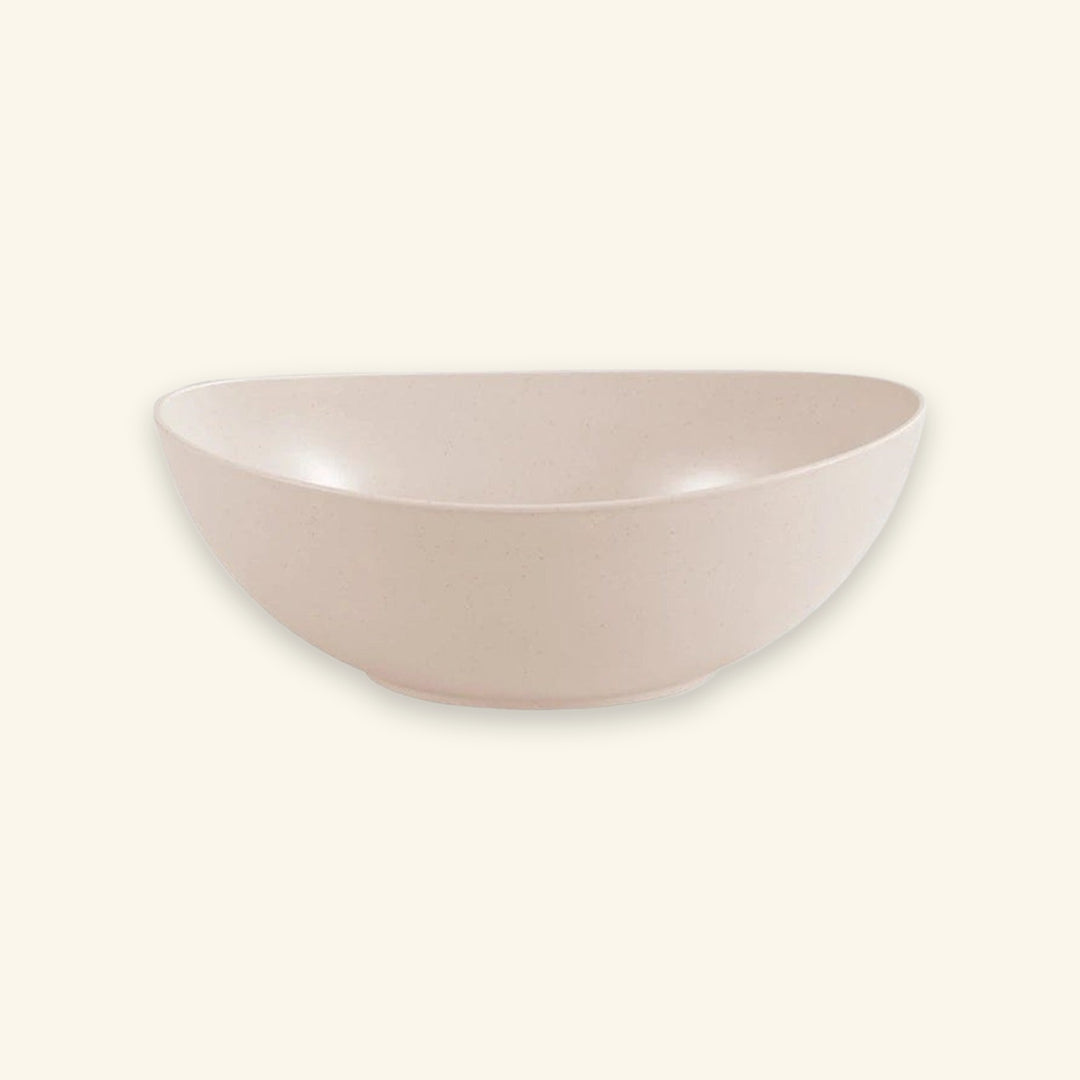 A minimalist, semi-circular ceramic bowl in a light blush pink color with subtle speckled texture, set against a solid cream background.