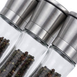 Three clear glass pepper mills with brushed stainless steel caps, shown close-up with peppercorns visible inside, on a white background.