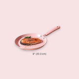 An 8-inch round frying pan with a pink interior and a light pink handle, shown on a pale pink background with a salmon fillet cooking inside. The text '8" (20.