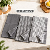 Three folded gray kitchen towels with different patterns are displayed on a light marble countertop. The left towel is solid gray, the middle towel has thin white vertical stripes, and the right towel has a gray and white gingham check pattern.