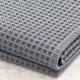 A folded gray and white textured fabric, likely a throw blanket or woven textile, displayed on a light marble surface.