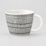 A white ceramic mug with a black hand-drawn vertical stripe pattern, shown against a neutral light gray background.