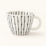 A white ceramic coffee mug with a black vertical drip pattern, shown on a clean white background.