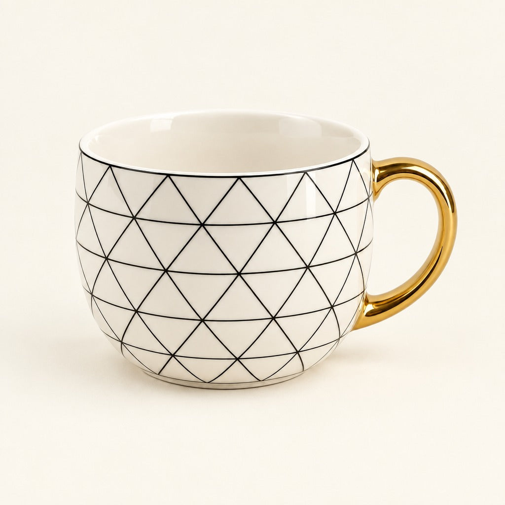 A white ceramic coffee mug with a black geometric diamond pattern and a shiny gold handle, set against a plain cream background.