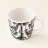 A white ceramic mug with a black vertical stripe grid pattern on the exterior, shown on a light cream background.