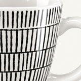 Close-up of a white ceramic mug with a black hand-drawn vertical stripe pattern, showing the side and handle against a light background.