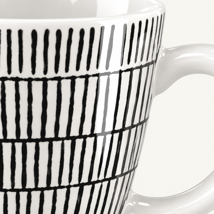 Close-up of a white ceramic mug with a black hand-drawn vertical stripe pattern, showing the side and handle against a light background.